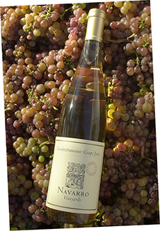 A bottle of Navarro Gewürztraminer grape juice laying on fresh Gewürztraminer grapes.