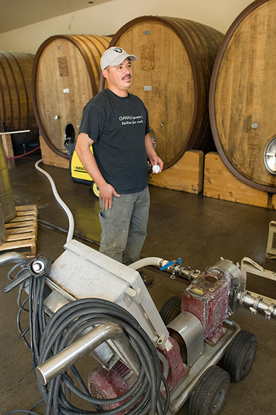 Alfredo operating a pump in front of several large oak wine ovals.