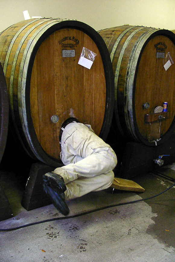 A smaller oak cask, about 200 gallons, with a winery worker squeezing inside to clean.