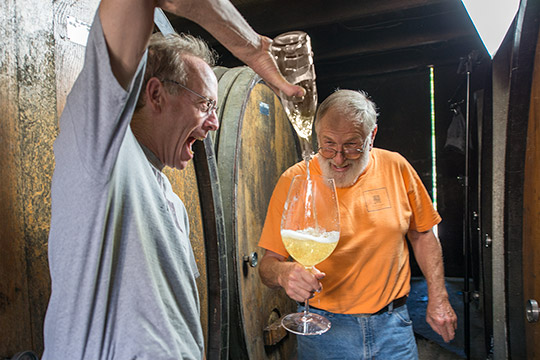 Ted and Jim laughing while pouring into a rediculously sized glass of wine.