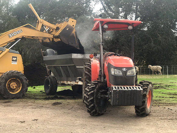 Loading compost into a spreader hauled behind a tractor.